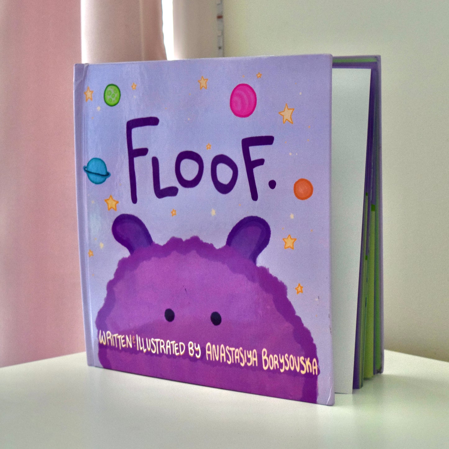 Story book side angle, with a purple alien Floof peeking on the cover.